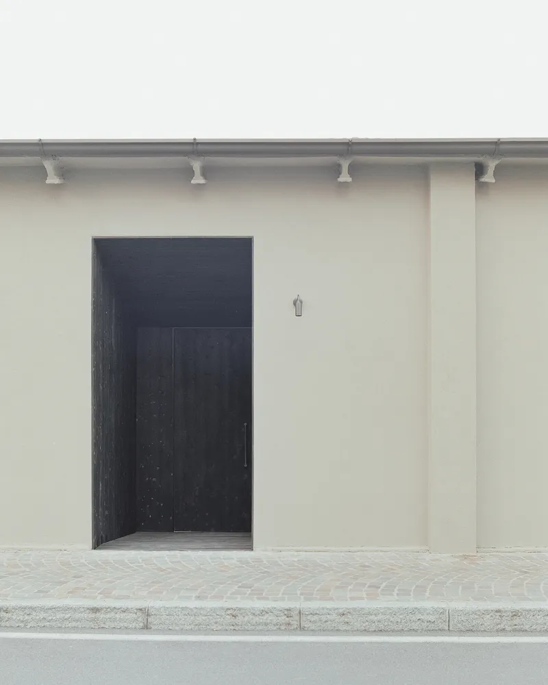 Black timber entry door set into smooth stucco wall with decorative terracotta corbels at the roofline