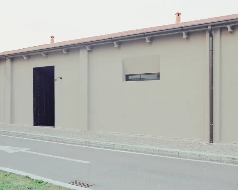 Street facade with recessed black timber door, narrow window and terracotta tile eaves under overcast sky