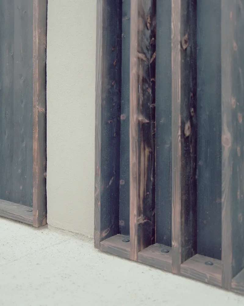 Close-up detail of charred timber battens meeting the rendered plaster at floor level