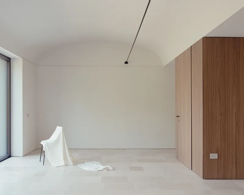 Interior room with vaulted ceiling, pale timber floor, walnut cabinetry and a draped cloth on a chair
