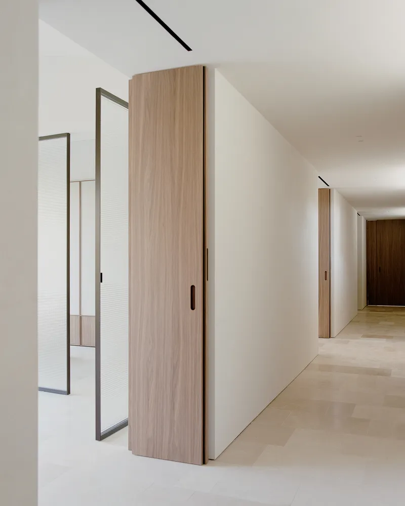 Corridor view showing walnut sliding doors, metal-framed reeded glass partition and recessed ceiling track