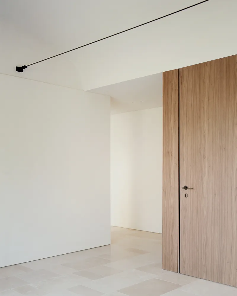 Interior corner with flush walnut door, white walls and linear black ceiling track lighting
