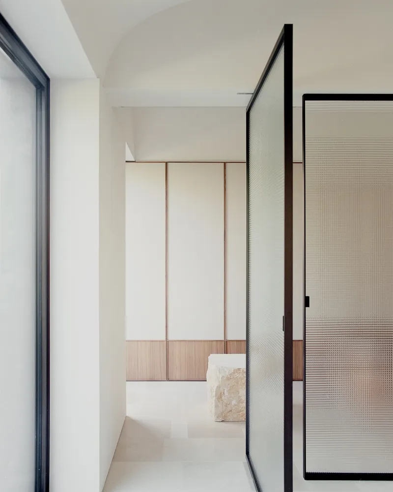 Hallway threshold with black-framed reeded glass door and timber bench beneath a vaulted ceiling