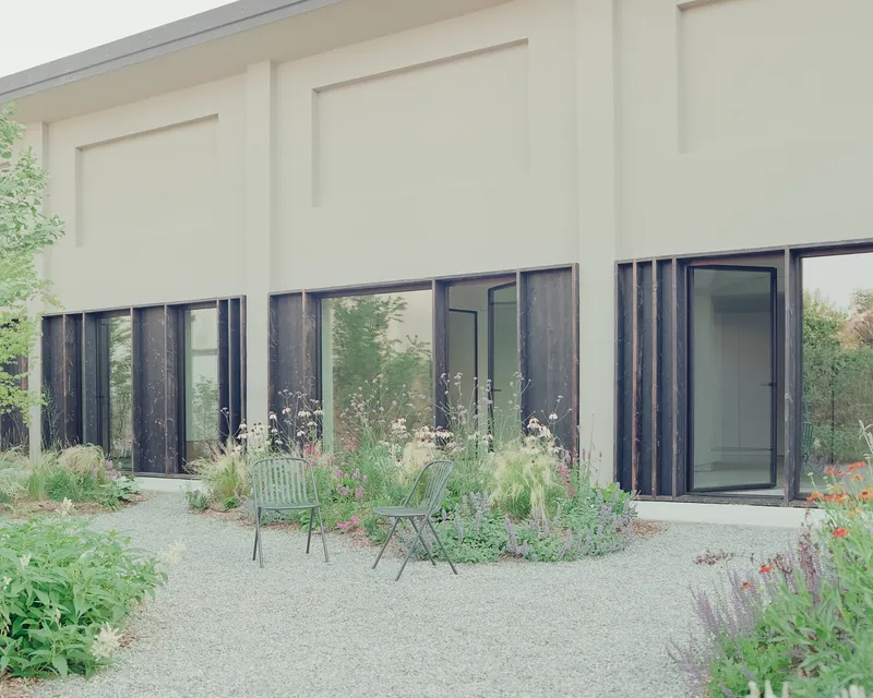 Garden courtyard with gravel path, planted beds and charred timber framed doors beneath a paneled facade