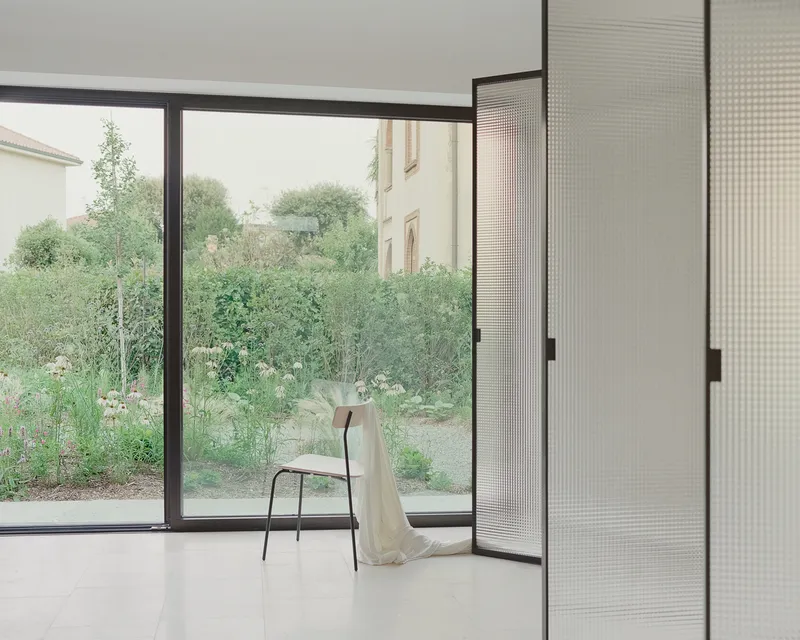 Corner window overlooking a garden with a single chair draped in fabric on polished floor