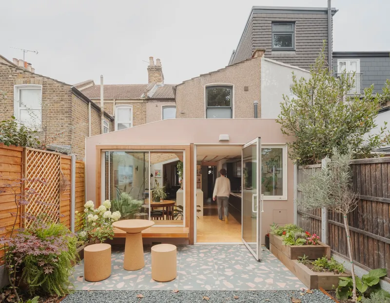 Rear garden view of the pink-toned extension with sliding glass doors and terrazzo paving under overcast sky