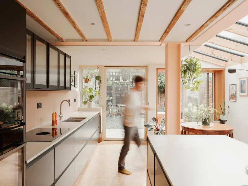 Kitchen interior with figure in motion passing between white countertop island and dark cabinetry
