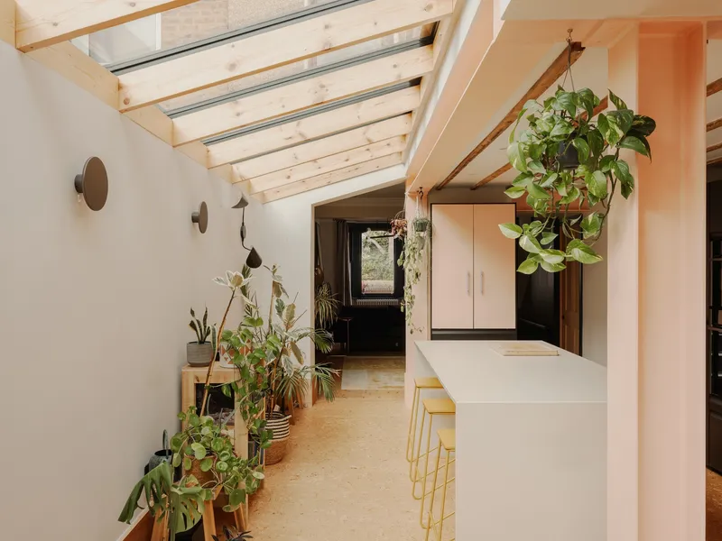 Skylit circulation space with potted plants lining timber shelf beneath exposed rafters and steel beams
