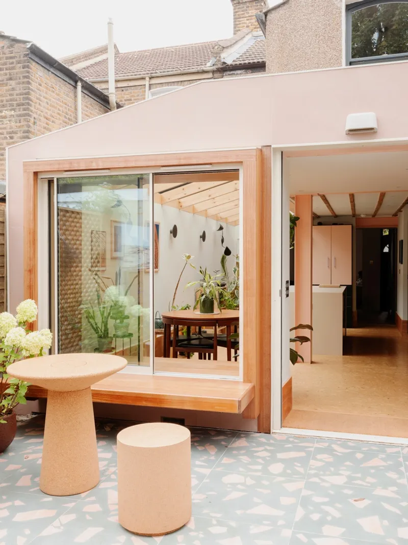 Open sliding glass doors revealing the dining area with exposed timber ceiling joists and potted plants