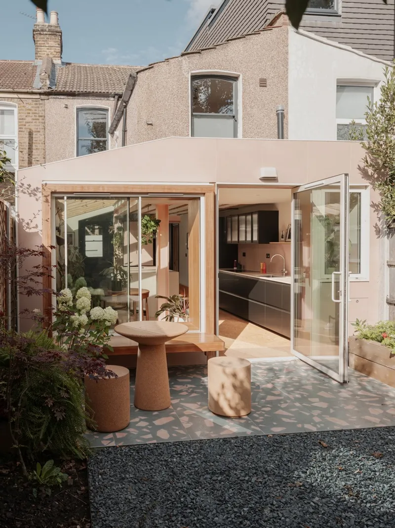 Garden courtyard with terrazzo paving and cork stools beneath the angled roof of the extension