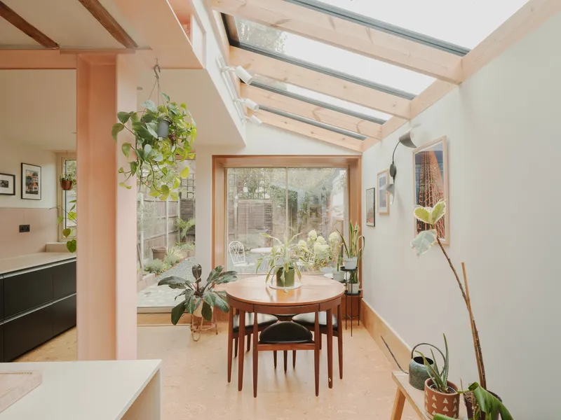 Dining area beneath exposed timber rafters and skylights with potted plants around a circular table