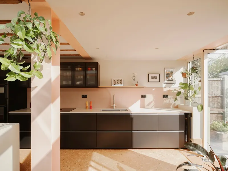 Kitchen with dark cabinetry and white countertop under an open timber stair and hanging plants