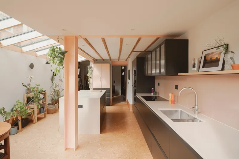 Galley kitchen with exposed timber beams and skylights overlooking a planted shelf and courtyard beyond