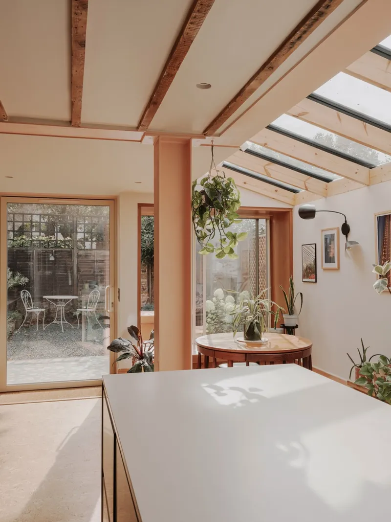 Kitchen island and dining table framed by timber columns with glazed doors opening to a gravel courtyard