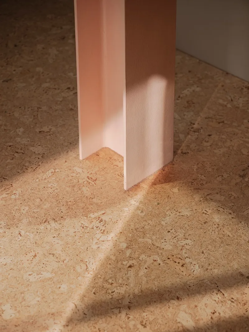 Base of a pink timber column meeting a cork floor with dappled sunlight