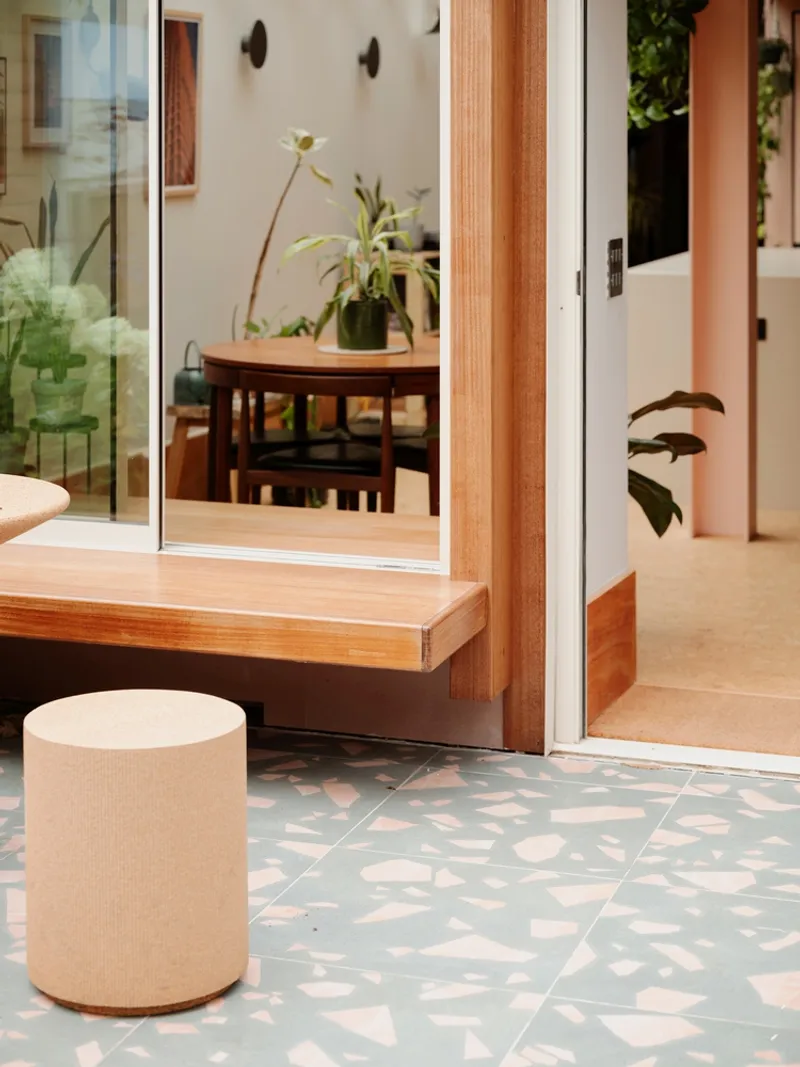 Threshold between interior and courtyard showing timber sliding door frame and terrazzo paving with hanging plants