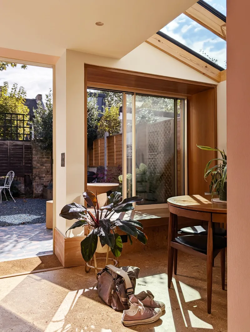 Interior corner with timber-framed bay window overlooking courtyard and morning sunlight on cork flooring