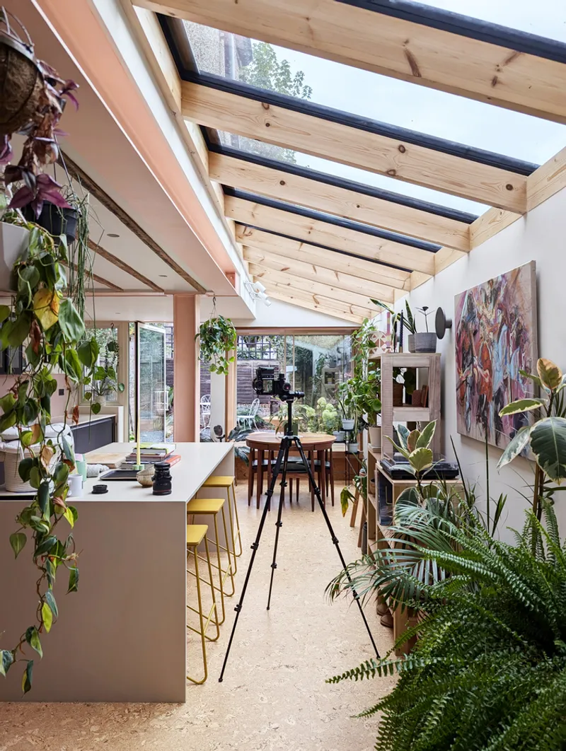 Open-plan kitchen and dining space with exposed timber rafters and abundant potted plants