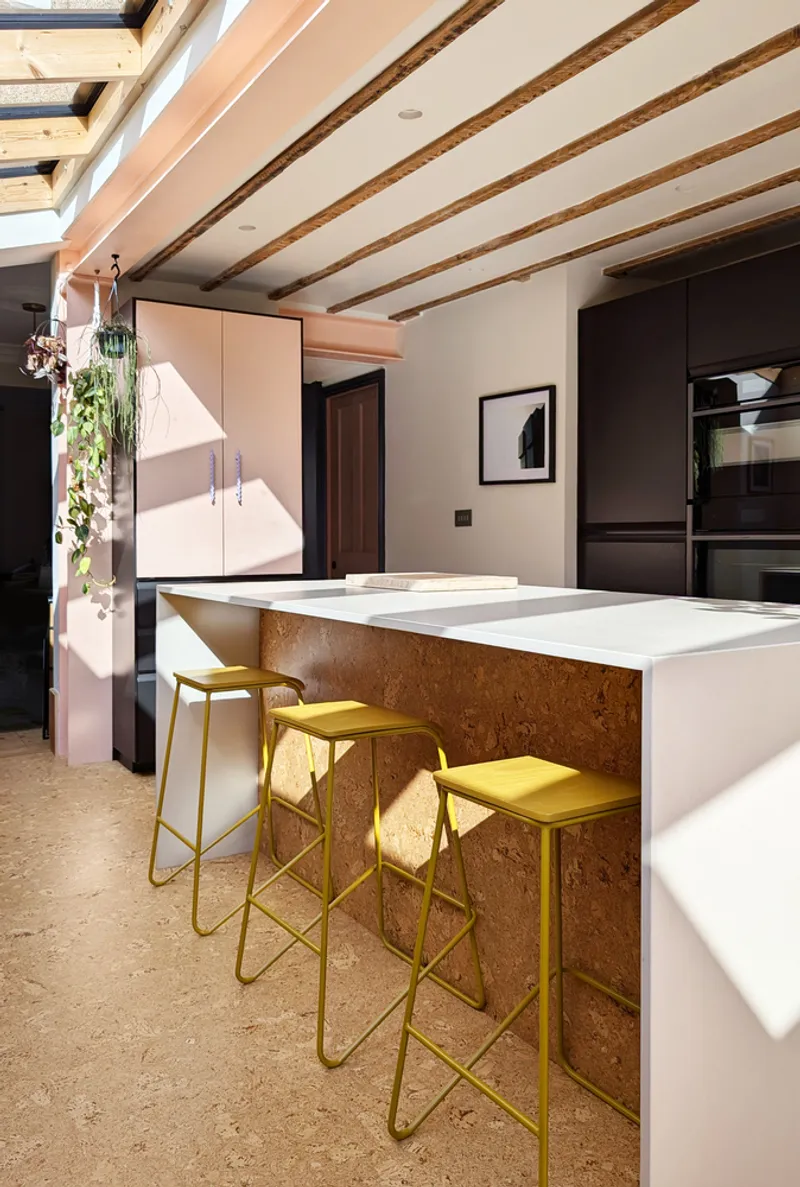 Kitchen island with cork-clad side and exposed timber ceiling beams under a skylight