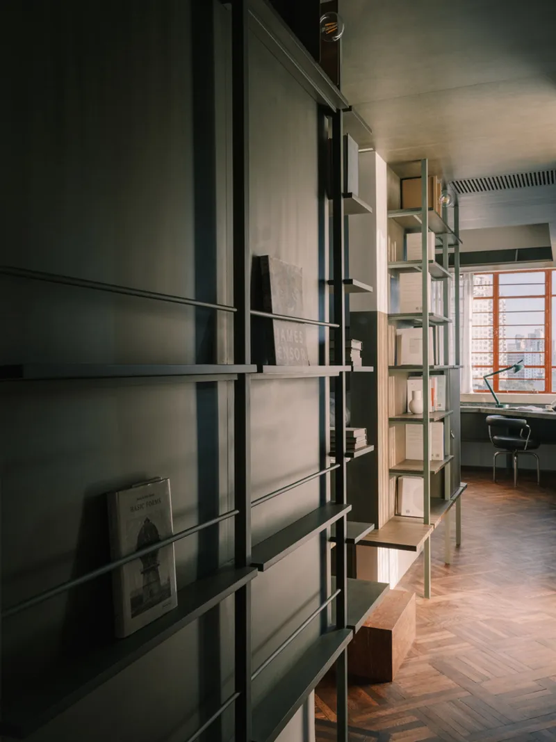 Metal shelving system with dark green framework dividing rooms with herringbone wood floors and desk beyond