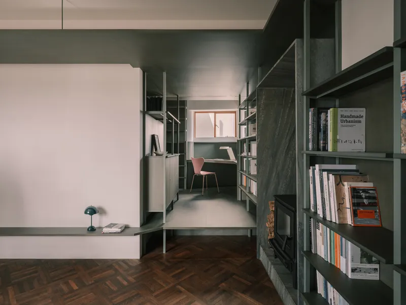 View through white partition opening into study area with green shelving and pink chair at desk