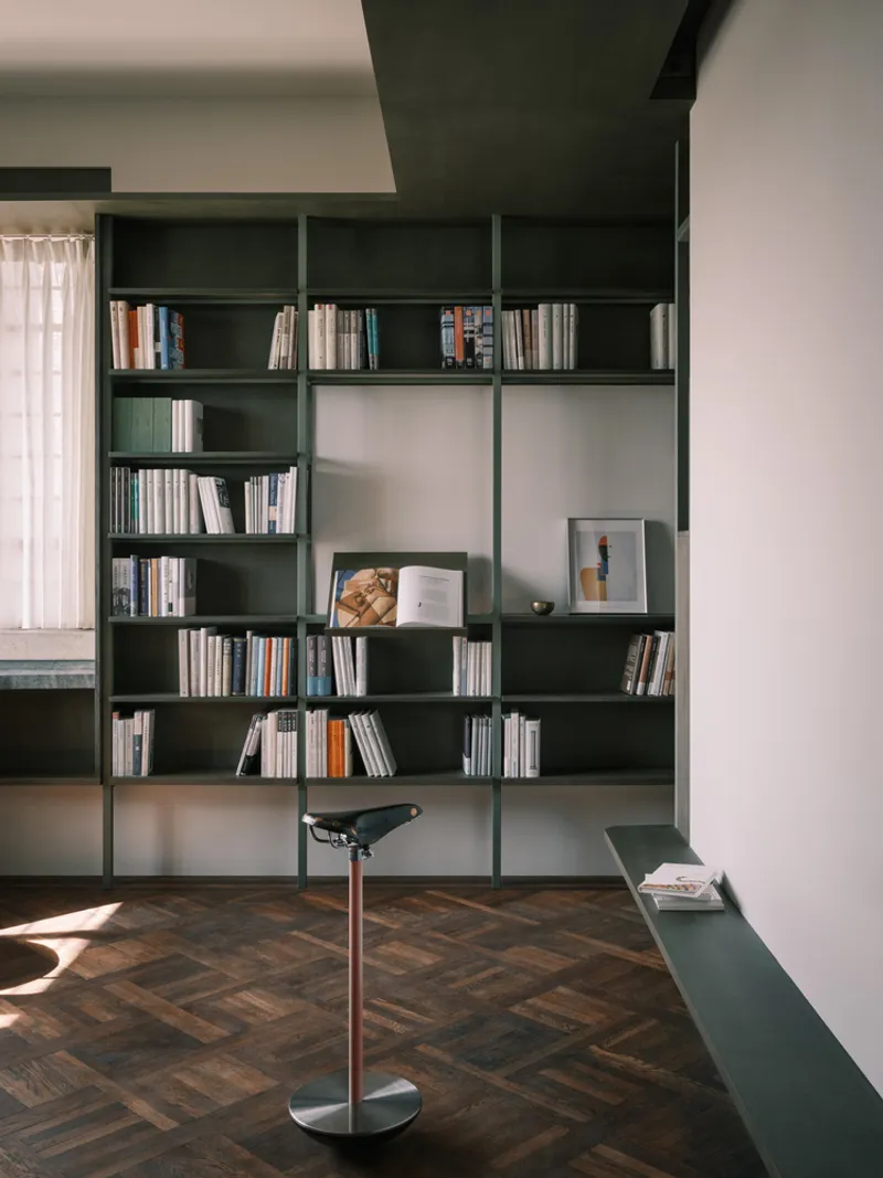 Dark green modular shelving wall with open and closed compartments above herringbone wood flooring in natural light