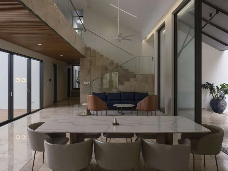 Double-height living space with cantilevered stone staircase, glass balustrade, and timber ceiling above dining area