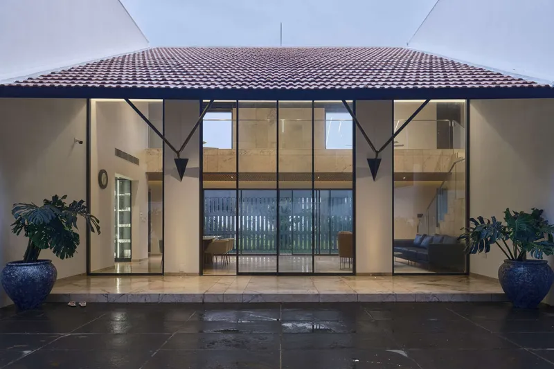 Covered entry terrace with terracotta tile roof, full-height glass doors, and glazed planters flanking wet paving