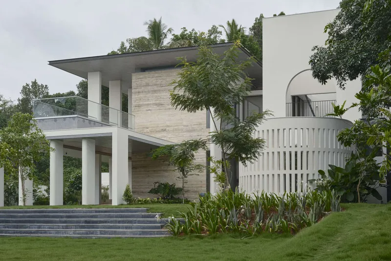 Front facade with white columns, vertical timber cladding, and vertical slatted screens framed by mature trees