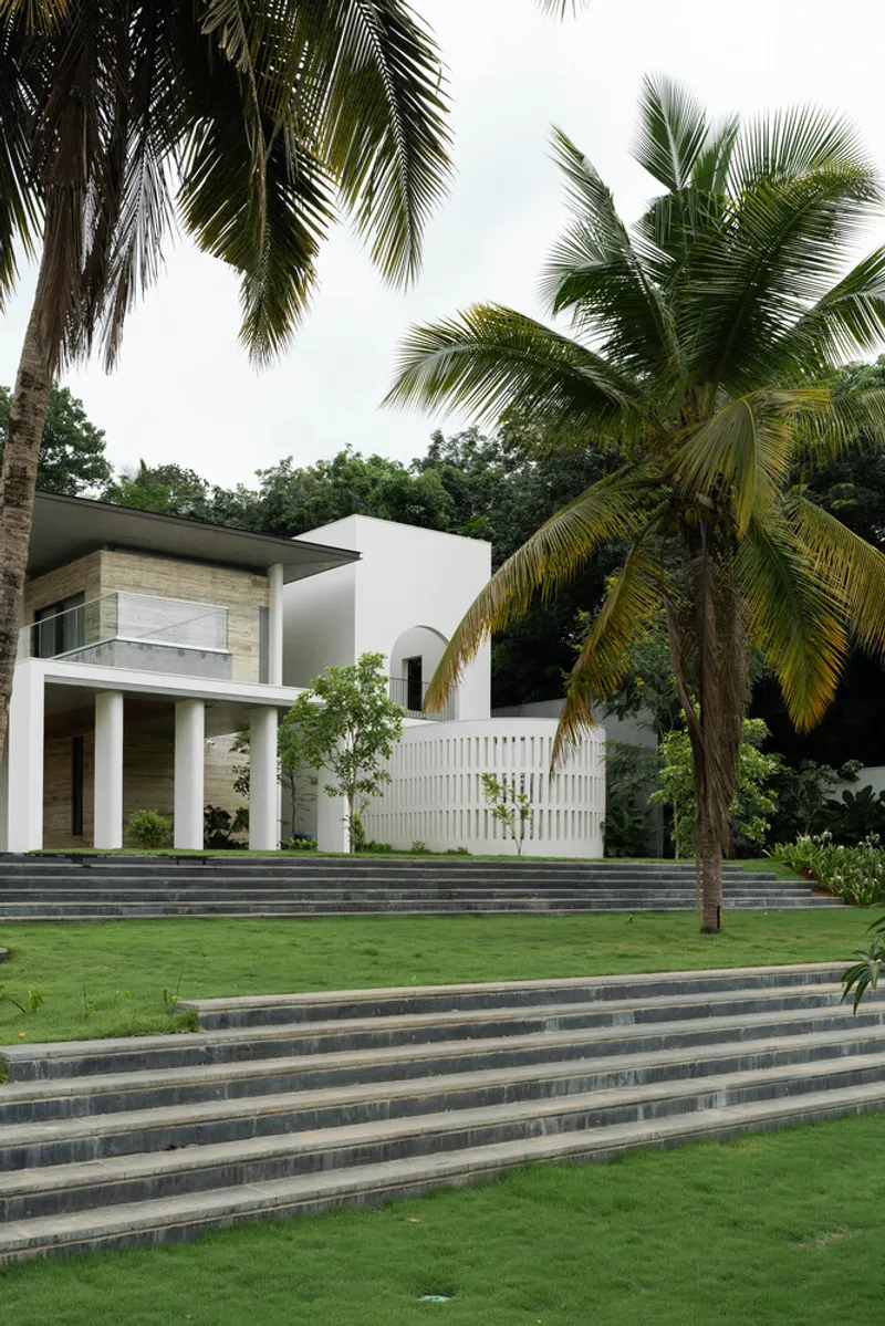 Terraced lawn with striped stone steps leading to white facade and vertical screen beneath coconut palms