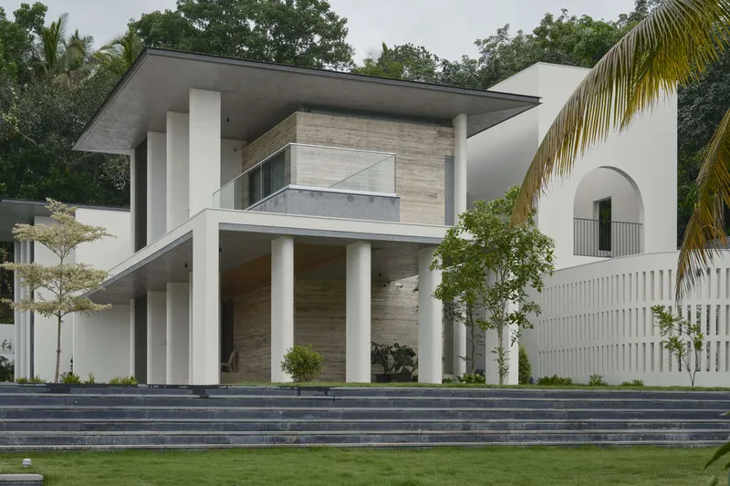 Front facade with cantilevered concrete roof and white columns framing the entry beneath palm trees