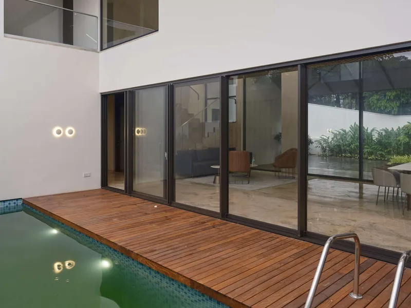 Timber deck alongside a green-tiled pool with sliding glass doors opening to the interior at dusk