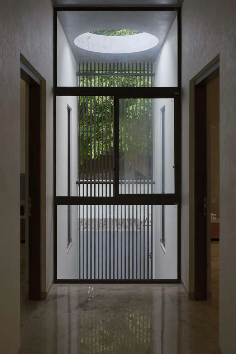 Entry corridor framing a courtyard with vertical slat screen and bamboo beyond an oval skylight above