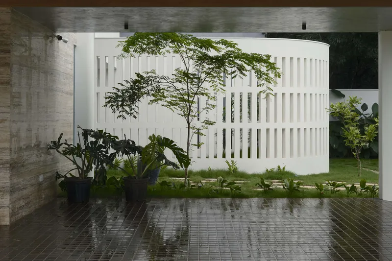 Covered terrace with wet brick pavers and potted plants facing a white slatted screen wall