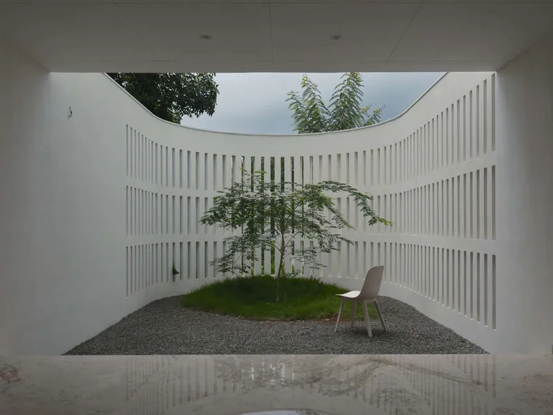 Interior courtyard with curved white slatted walls framing a single tree and white chair on gravel