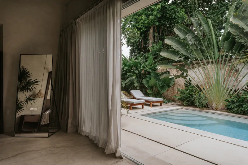 Sheer curtains framing a small pool deck surrounded by banana plants and tropical vegetation