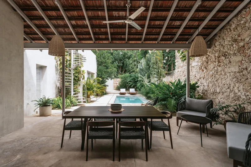 Covered dining terrace with timber ceiling looking toward the pool and lush planted garden
