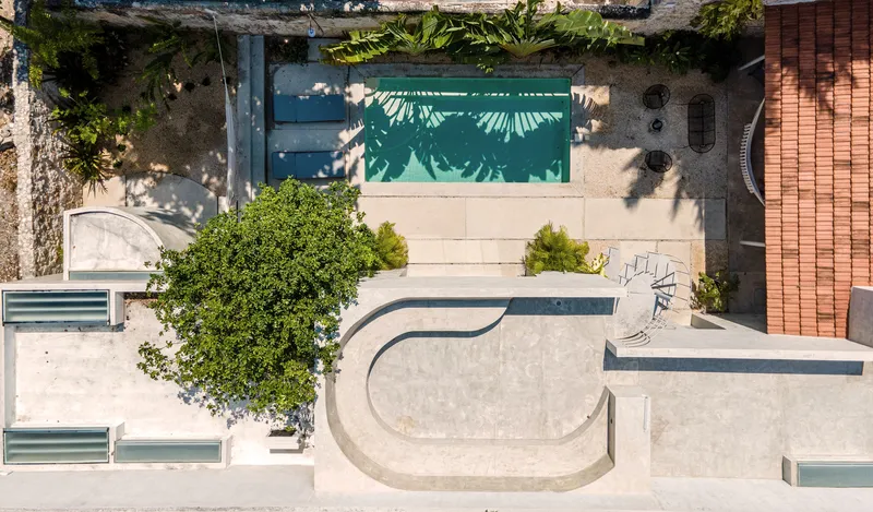 Drone view showing the pool, tree canopy, and stepped courtyard surrounded by stone and plastered walls