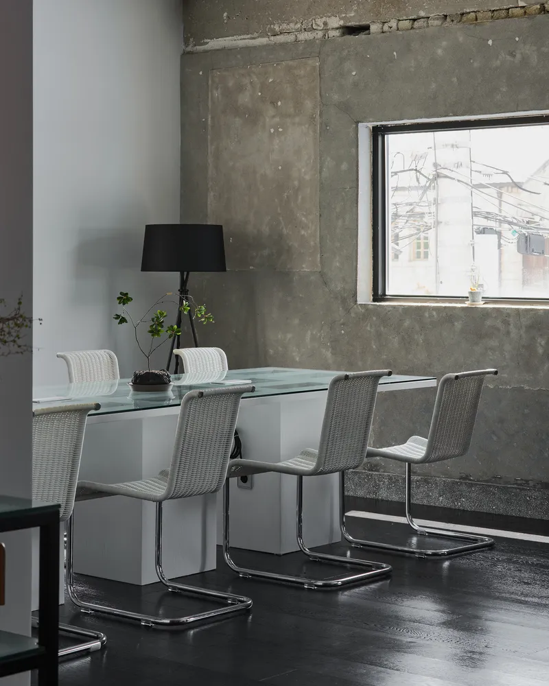 Dining area with glass table and cantilever chairs against a weathered concrete wall with potted plants