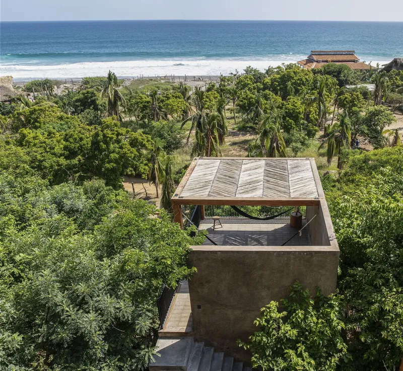 Aerial view of the timber pavilion roof nestled among palms and tropical vegetation near the ocean