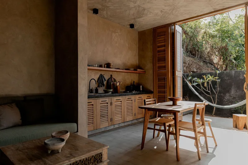 Living area with louvered kitchen cabinetry and dining table facing the garden courtyard and curved wall