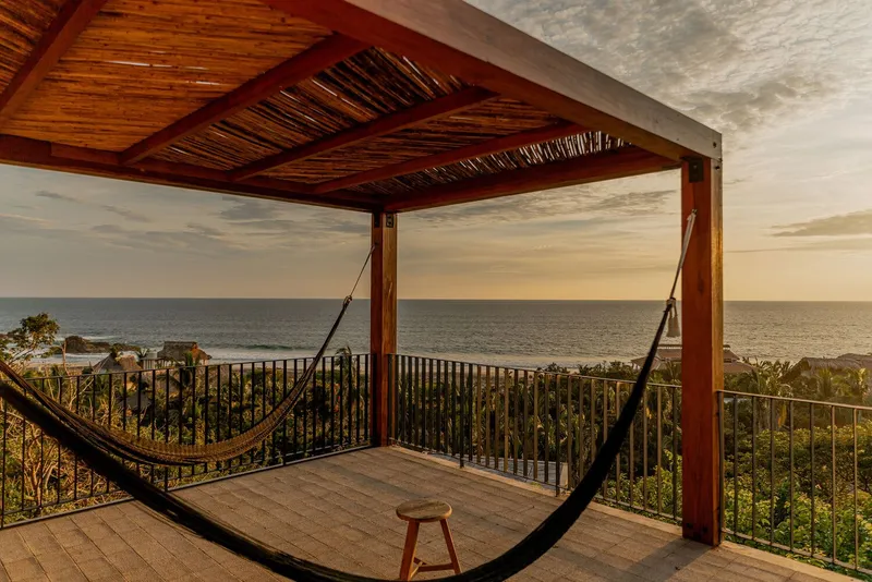 Upper terrace with timber pergola, metal railing and hammock overlooking the ocean at dusk