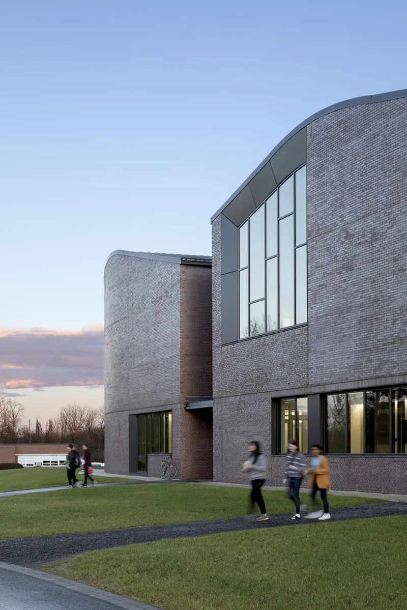 Curved brick facade with vertical glazing and students walking along the pathway at twilight
