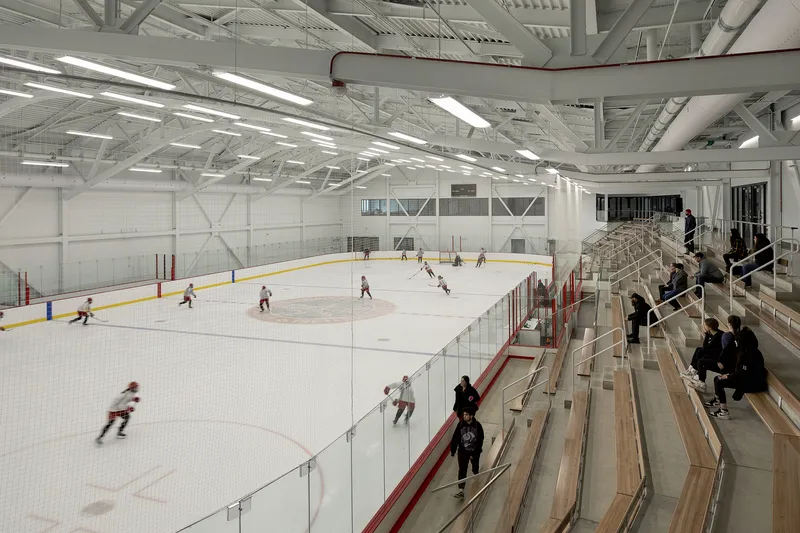 Ice hockey rink with white steel truss ceiling and spectators on timber bleachers