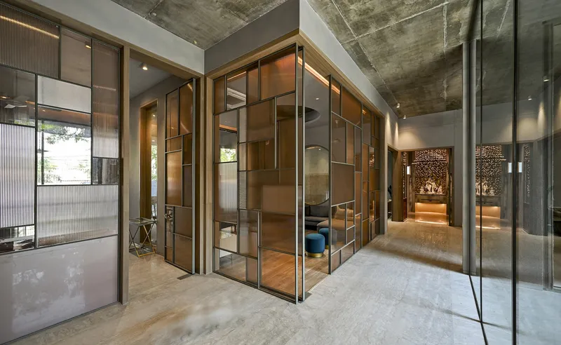 Interior hallway junction with folding bronze-framed glass doors under an exposed concrete ceiling