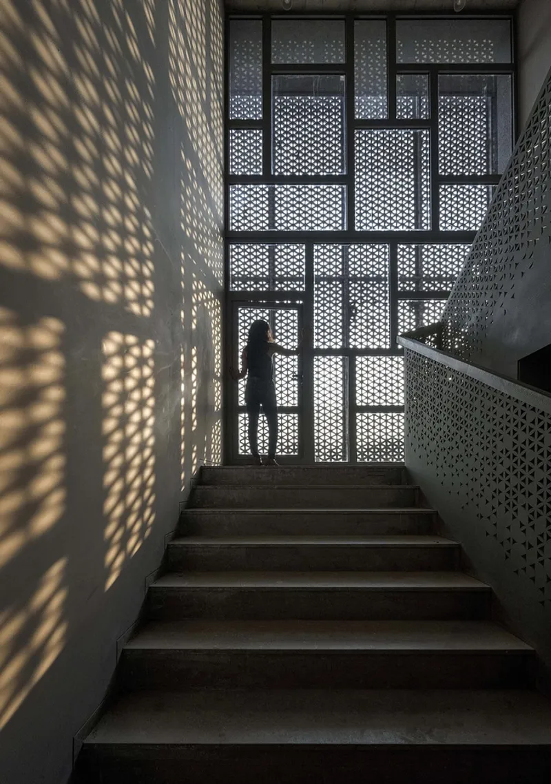 Staircase enclosed by perforated metal panels casting geometric shadow patterns across dark steps and walls