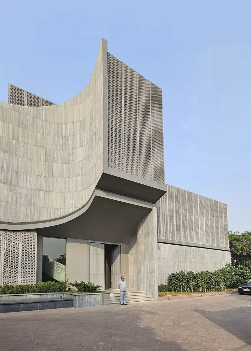 Entry facade with curved stone-clad wall and perforated metal tower against a clear blue sky