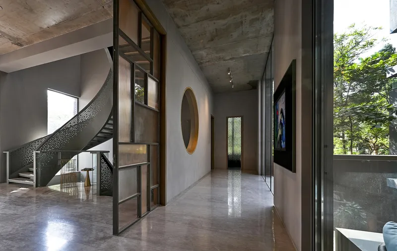 Interior gallery corridor with curved perforated metal stair, circular portal opening, and exposed concrete ceiling