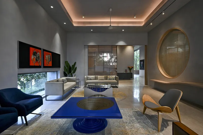 Double-height living room with recessed cove lighting and circular mirror set into grey walls