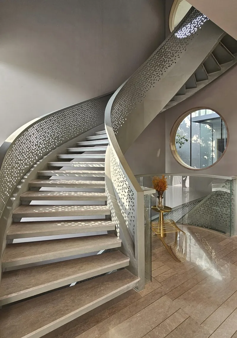 Curved staircase with perforated metal balustrade ascending past a circular wood-framed mirror